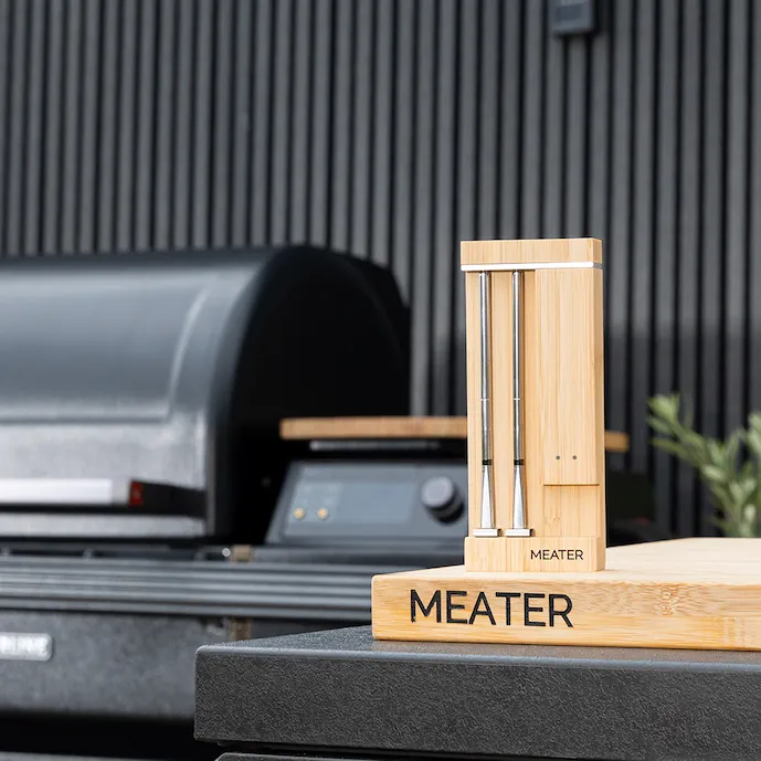 meater-fleischthermometer-auf-einem-schneidbrett-im-hintergrund-ein-traegergrill